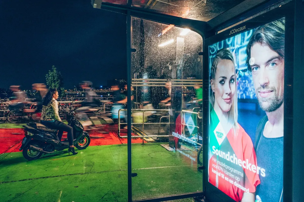 companies display ads on digital billboards on the sidewalk as woman rides by on a motorbike