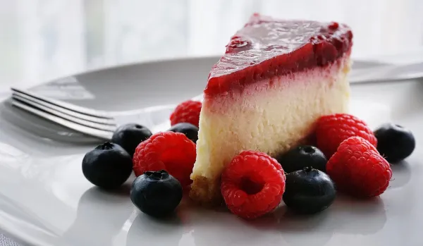 cheesecake dessert on a plate with blueberries and raspberries around the slice on a white plate